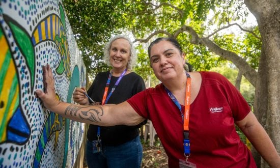 Two women add their handprints to an outdoor mural