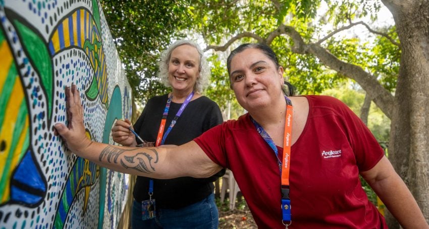 Two women add their handprints to an outdoor mural