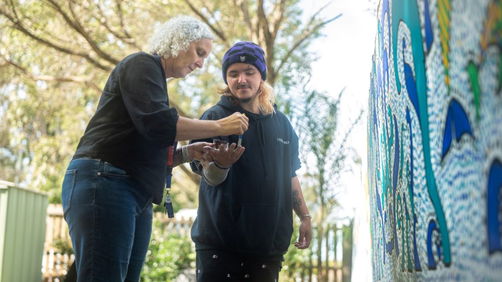 Two people add their handprints to an outdoor mural