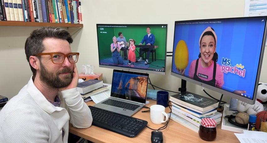 Man in white shirt in his office in front of three screens