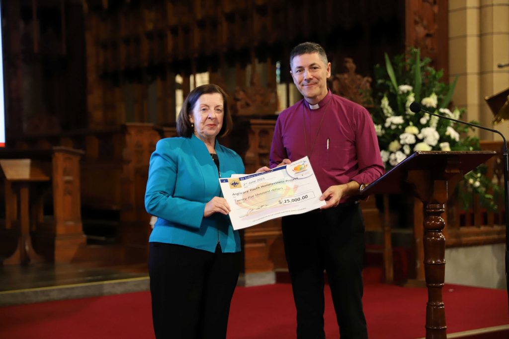 Two people stand holding a large novelty cheque in St John's Cathedral