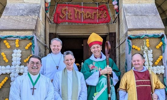 Five people standing outside a rural church, including an archbishop