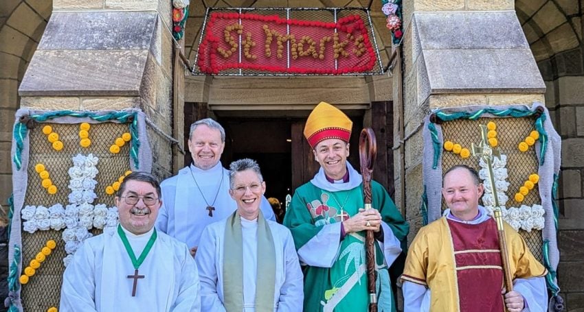 Five people standing outside a rural church, including an archbishop