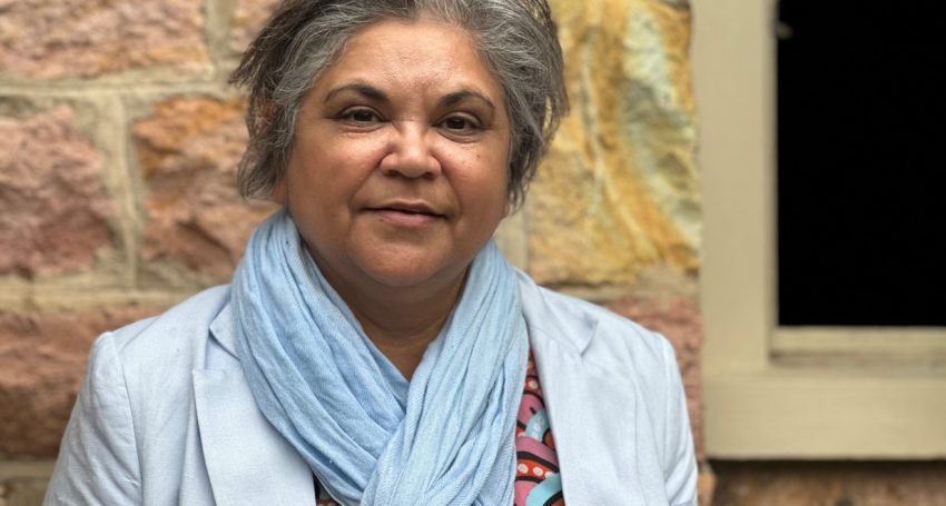 Woman in blue scarf and jacket looking at the camera with a soft smile