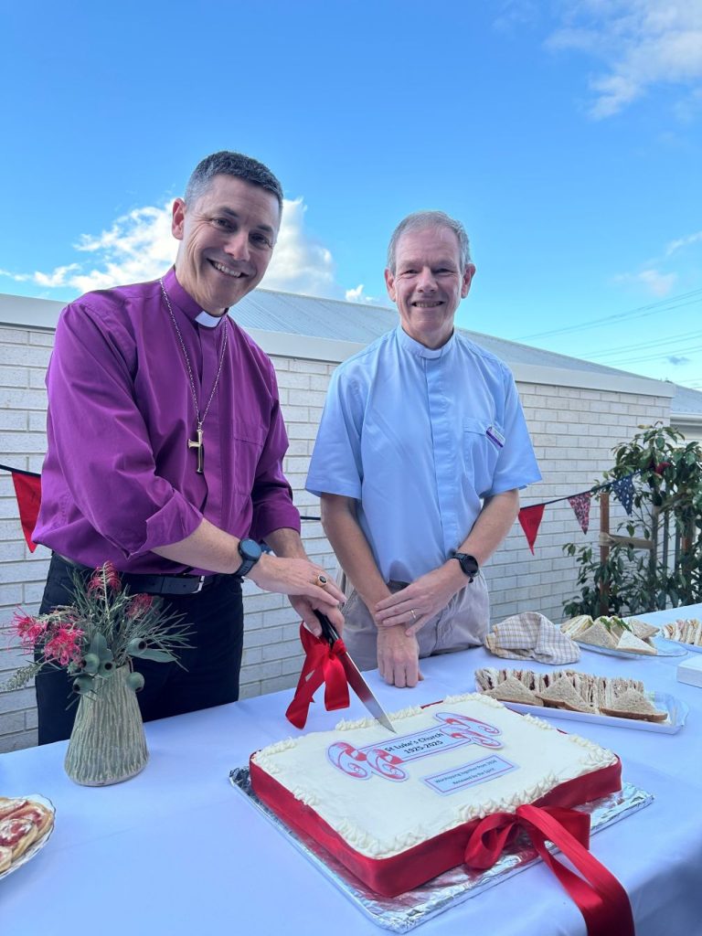 An Archbishop and a priest cutting a cake 