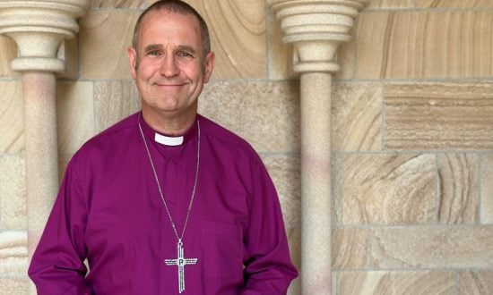Bishop in purple shirt and collar and pectoral cross outside a cathedral entrance