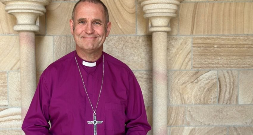 Bishop in purple shirt and collar and pectoral cross outside a cathedral entrance