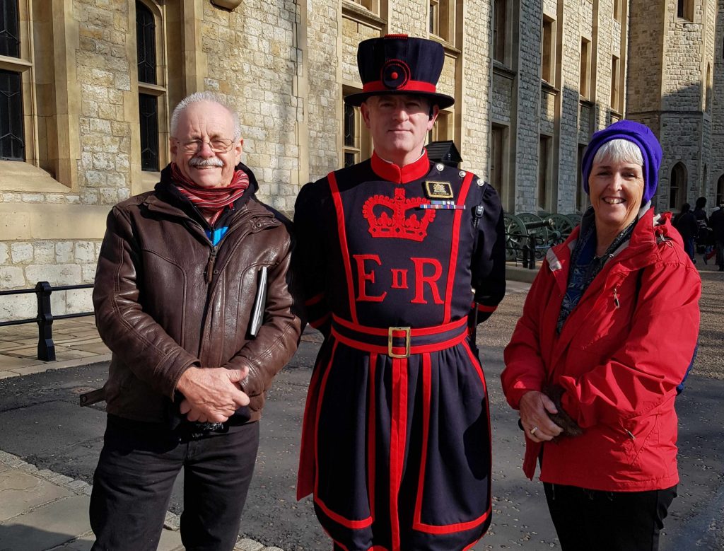 Two tourists pose for a photograph in London with a Tower of London Guard