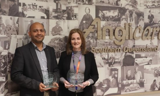 A man and a woman holding trophies next to an Anglicare sign