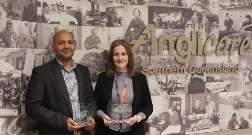A man and a woman holding trophies next to an Anglicare sign