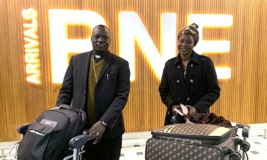 Two people pose for a photograph at an airport with luggage on trolleys