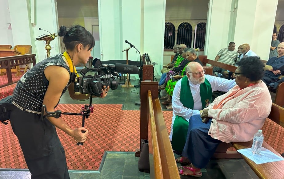 Woman with film camera filming a priest and elder in a church