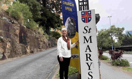 A woman stands outside posing for a photograph with a church banner