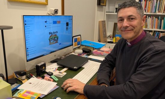 Archbishop in front of computer smiling