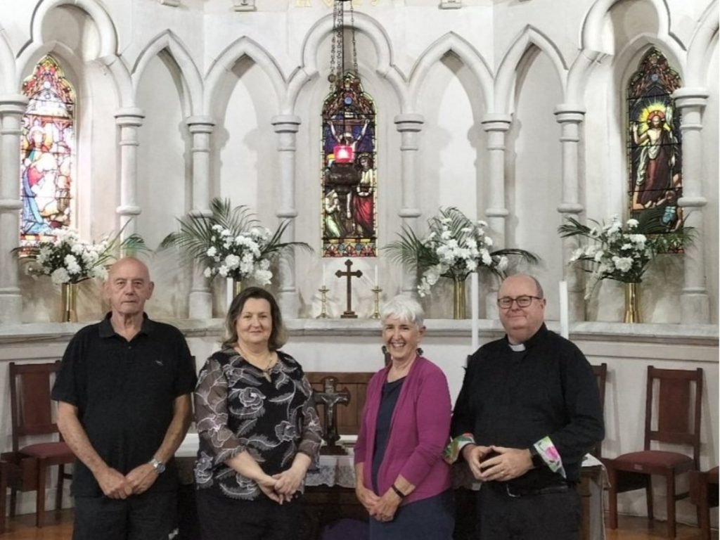 Four people stand inside a church posing for a photograph