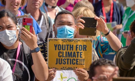 A group of climate protestors are gathered outside with one man holding a sign that reads "Youth for Climate Justice!"