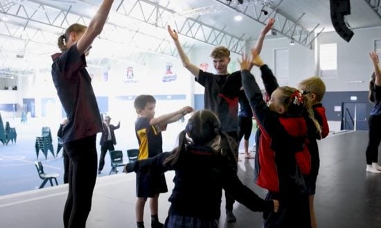 A group of students and a dance teacher are performing a dance routine in a large school hall