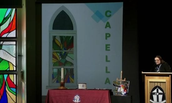 A woman stands in front of an image of chapel windows while speaking to an audience.