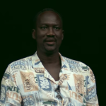 A man looks at the camera for an interview against a black background
