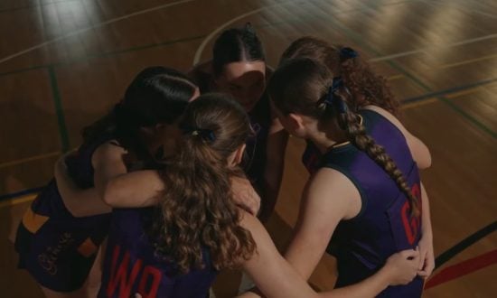 A group of students form a team huddle on a basketball court