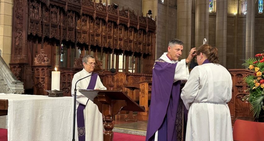 A priest in purple Lenten vestments applies ashes to a worshipper forehead during an Ash Wednesday 2026 service inside a cathedral